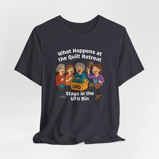 A A Heather Navy t-shirt featuring a cartoon design of four laughing women at a quilt retreat with a bin labeled “UFO” full of fabric. Surrounded by patchwork flying saucers and flowers. Text reads “What happens at the quilt retreat stays in the UFO bin.”