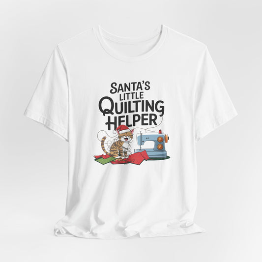 A White christmas quilting t-shirt featuring a playful cat wearing a Santa hat is tangled in thread next to a sewing machine, with the phrase "Santa's Little Quilting Helper" above, combining quilting and holiday humor.