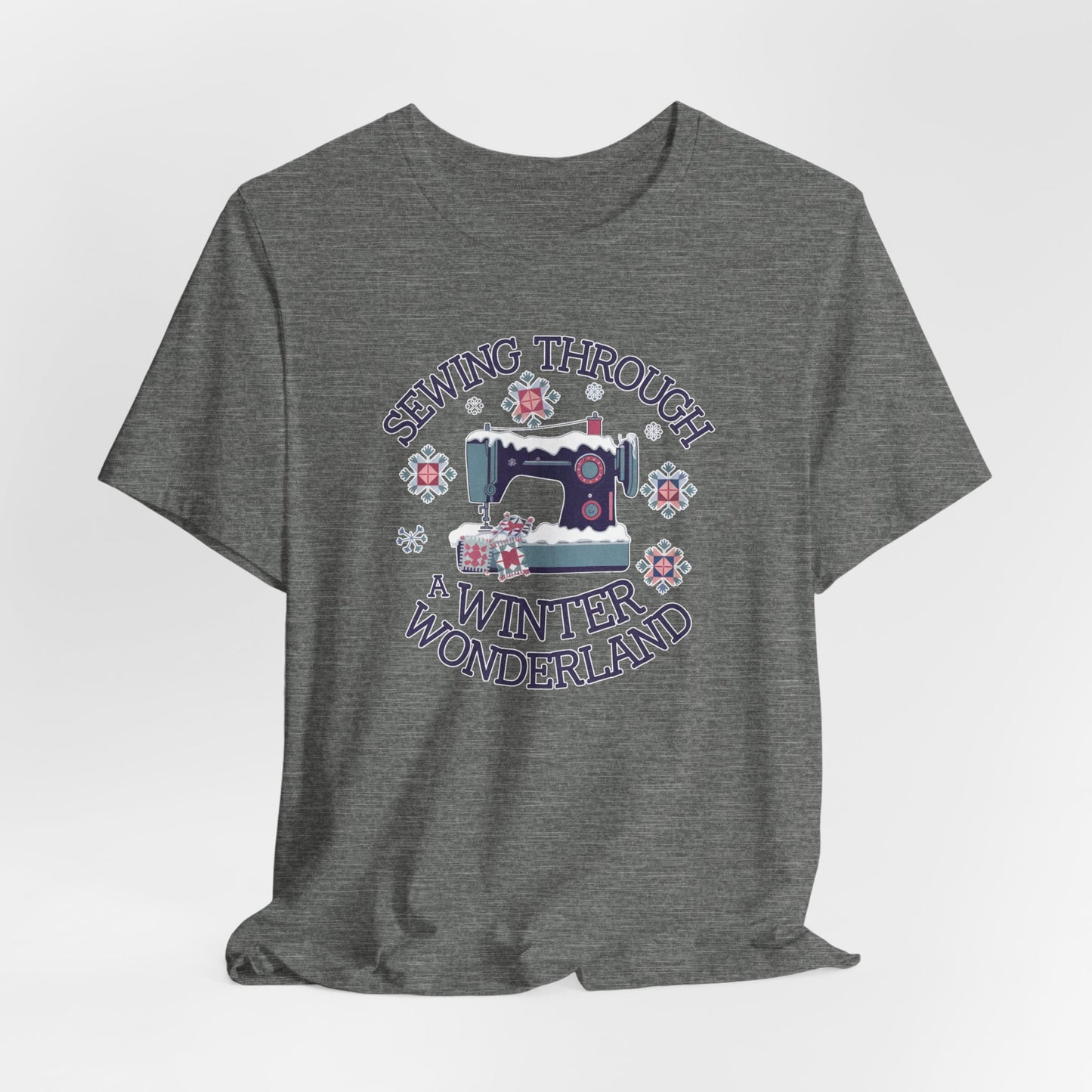 A Deep Heather winter quilting t-shirt featuring  a sewing machine covered in snow, surrounded by quilted snowflakes, with the phrase "Sewing Through a Winter Wonderland" above and below the image.