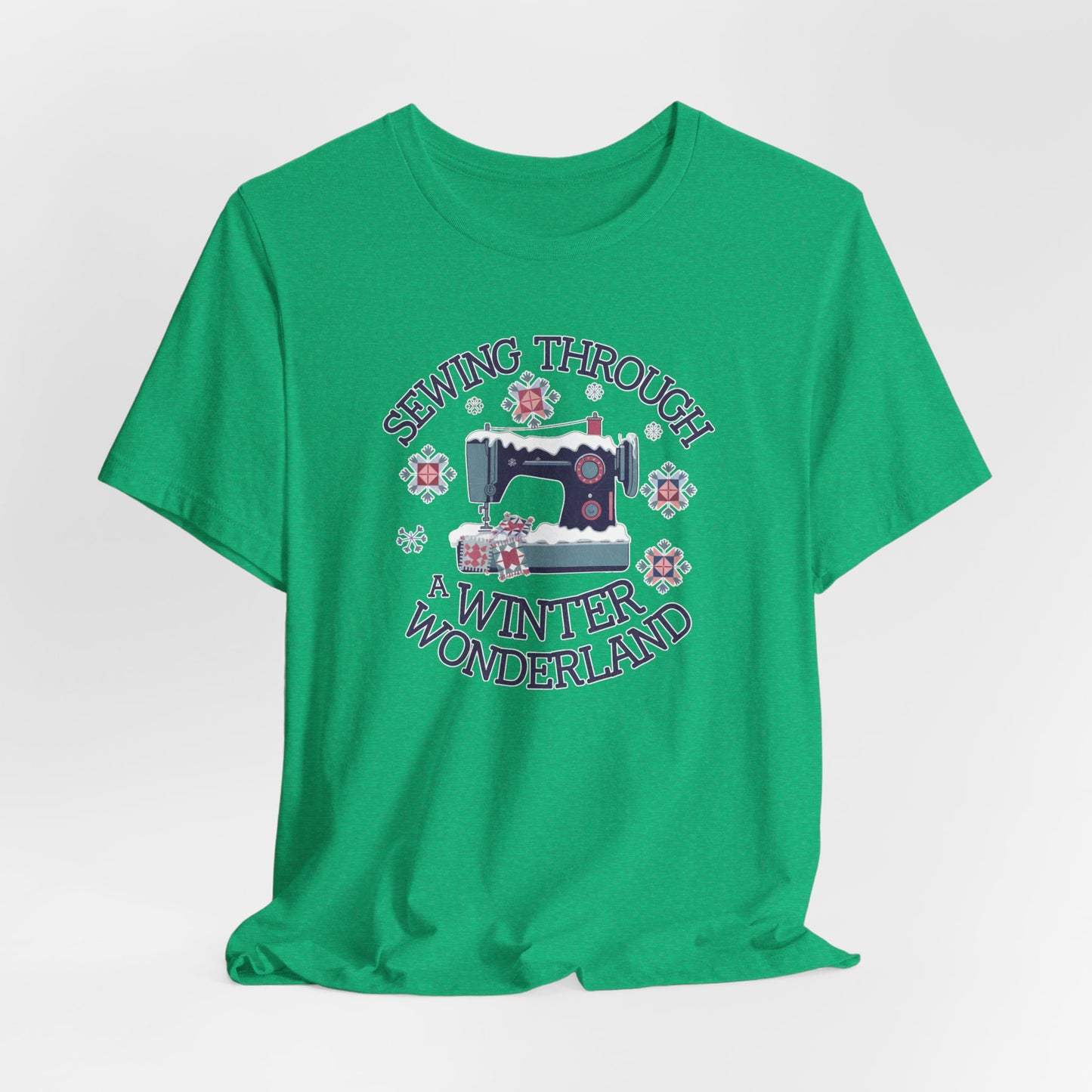 A Heather Kelly winter quilting t-shirt featuring  a sewing machine covered in snow, surrounded by quilted snowflakes, with the phrase "Sewing Through a Winter Wonderland" above and below the image.