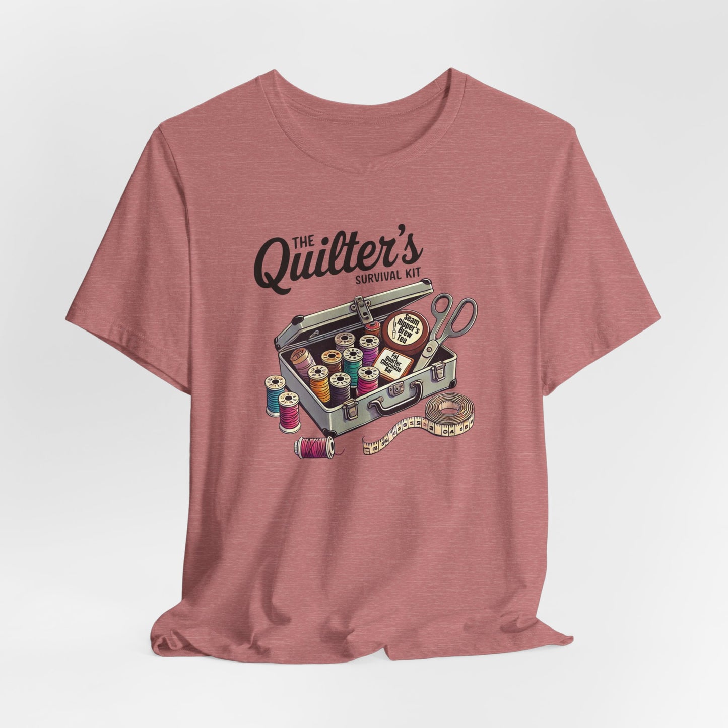 A Heather Mauve t-shirt featuring a whimsical illustration of a quilter’s survival kit with colorful thread spools, scissors, and a tape measure, perfect for sewing and quilting enthusiasts.