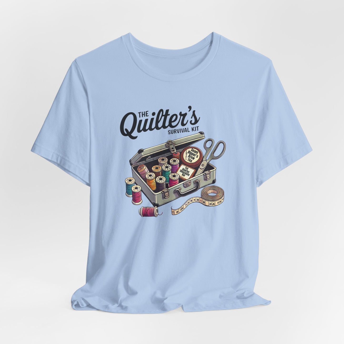 A Baby Blue t-shirt featuring a whimsical illustration of a quilter’s survival kit with colorful thread spools, scissors, and a tape measure, perfect for sewing and quilting enthusiasts.