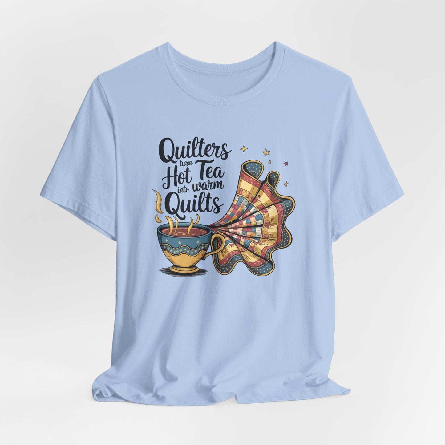 A Baby Blue t-shirt with a whimsical design of a teacup transforming into a patchwork quilt, accompanied by the phrase 'Quilters turn hot tea into warm quilts.' Ideal for quilters and tea lovers