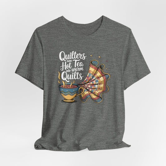 A Deep Heather t-shirt with a whimsical design of a teacup transforming into a patchwork quilt, accompanied by the phrase 'Quilters turn hot tea into warm quilts.' Ideal for quilters and tea lovers