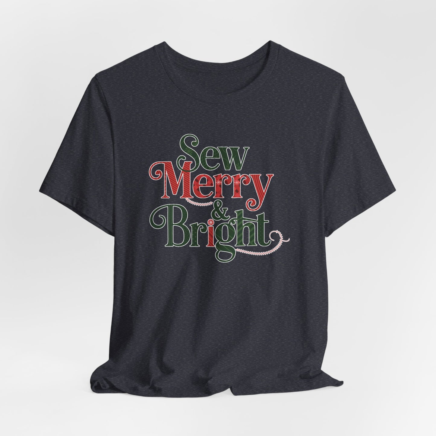 A Heather Navy t-shirt with the phrase "Sew Merry & Bright," incorporating sewing-inspired elements and holiday-themed accents, such as stitching lines and festive patterns.