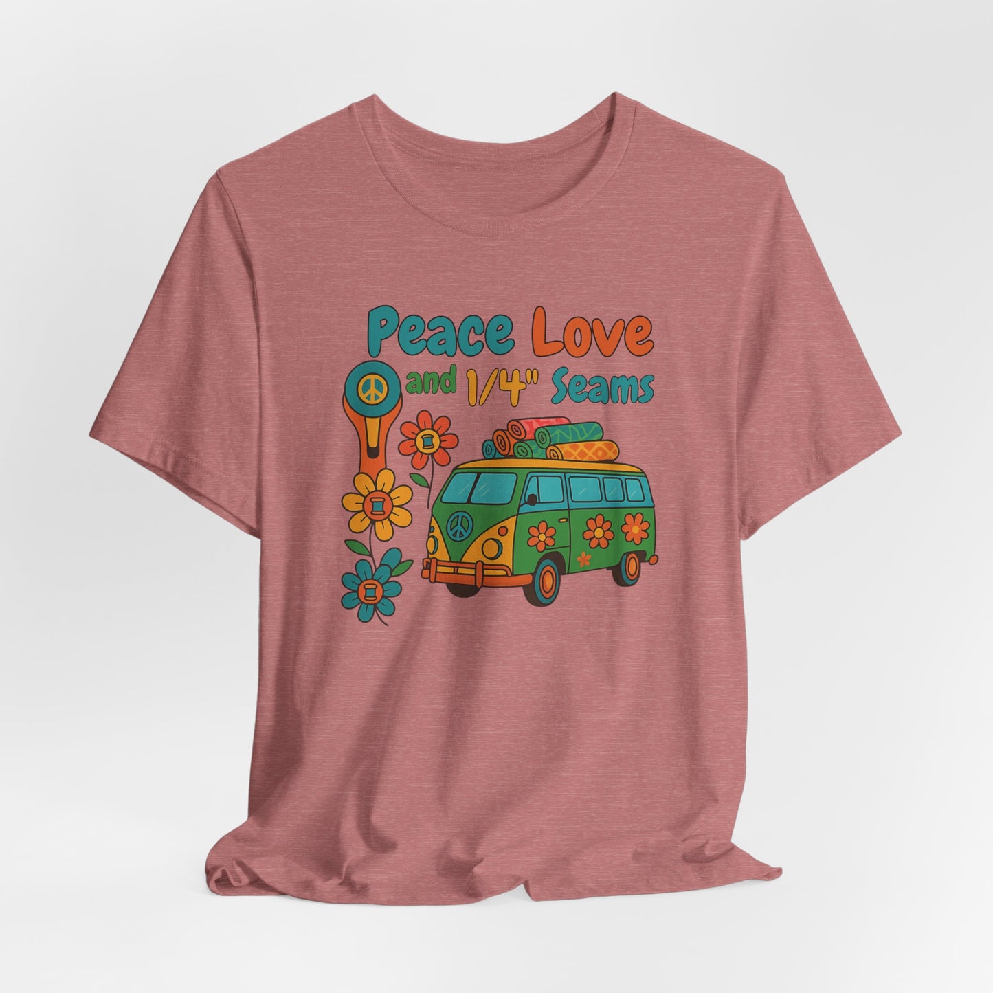 A A Heather Mauve t-shirt with colorful retro design showing a peace sign rotary cutter, patchwork van, and text “Peace Love and 1/4" Seams.” Surrounded by flowers made of thread spools. Fun vintage-style quilting shirt.