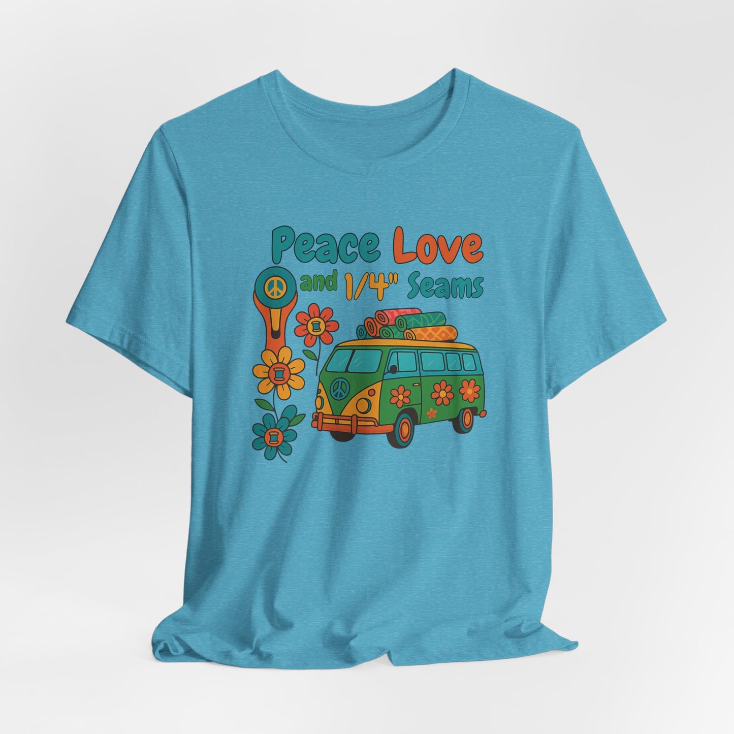 A A Heather Aqua t-shirt with colorful retro design showing a peace sign rotary cutter, patchwork van, and text “Peace Love and 1/4" Seams.” Surrounded by flowers made of thread spools. Fun vintage-style quilting shirt.