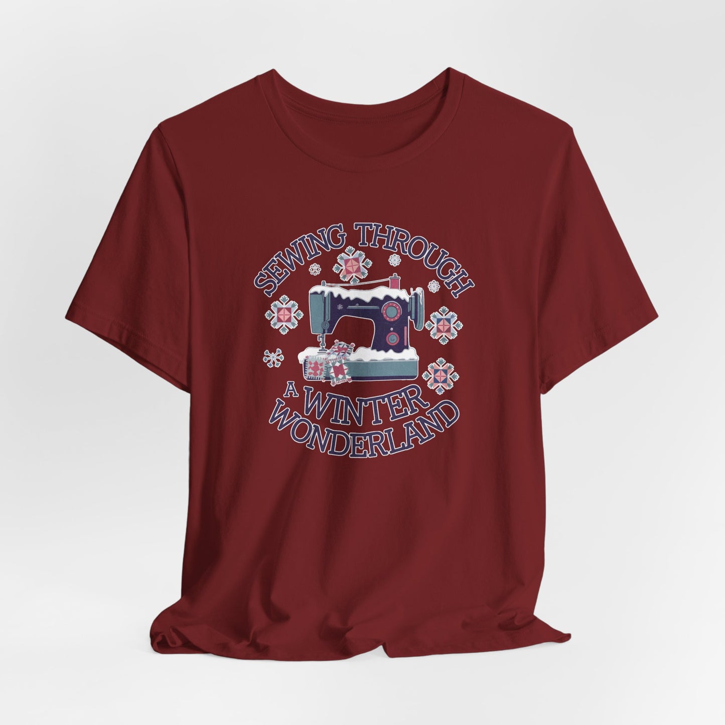 A Cardinal winter quilting t-shirt featuring  a sewing machine covered in snow, surrounded by quilted snowflakes, with the phrase "Sewing Through a Winter Wonderland" above and below the image.