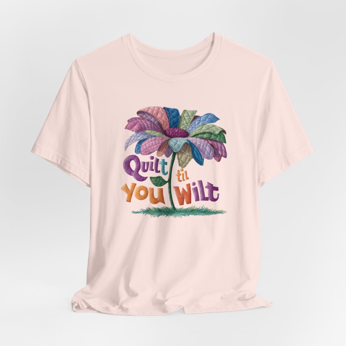 A Soft Pink funny quilting T-Shirt with the phrase Quilt 'Till You Wilt showing a cheerful, but slightly wilted quilted flower design