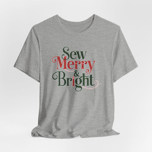 An Athletic Heather t-shirt with the phrase "Sew Merry & Bright," incorporating sewing-inspired elements and holiday-themed accents, such as stitching lines and festive patterns.