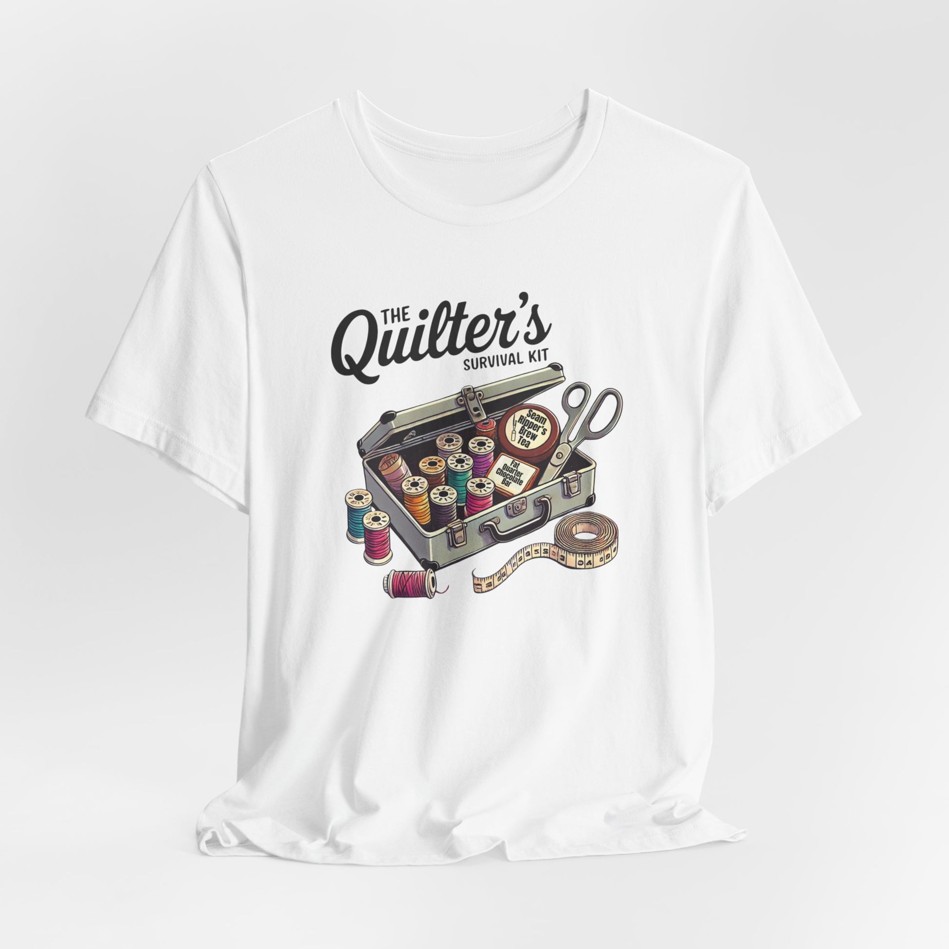 A White t-shirt featuring a whimsical illustration of a quilter’s survival kit with colorful thread spools, scissors, and a tape measure, perfect for sewing and quilting enthusiasts.