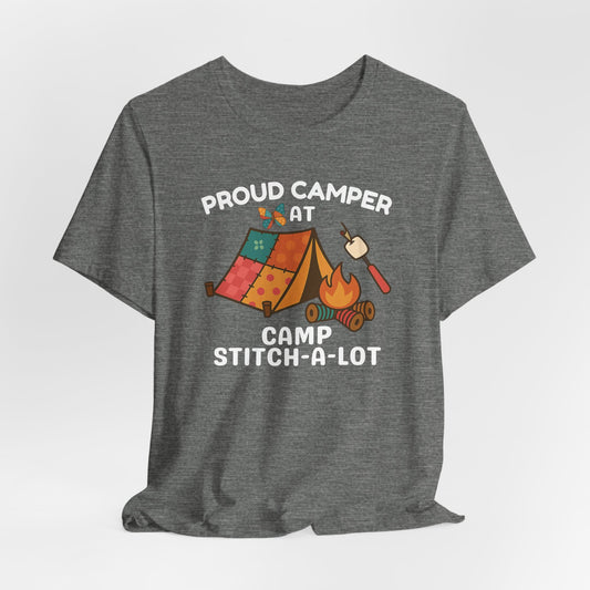 A A Deep Heather t-shirt featuring a colorful design with a patchwork tent, thread spool campfire, marshmallow on a seam ripper stick, and a butterfly. Text reads "Proud Camper at Camp Stitch-a-Lot." Fun gift for quilting retreats.