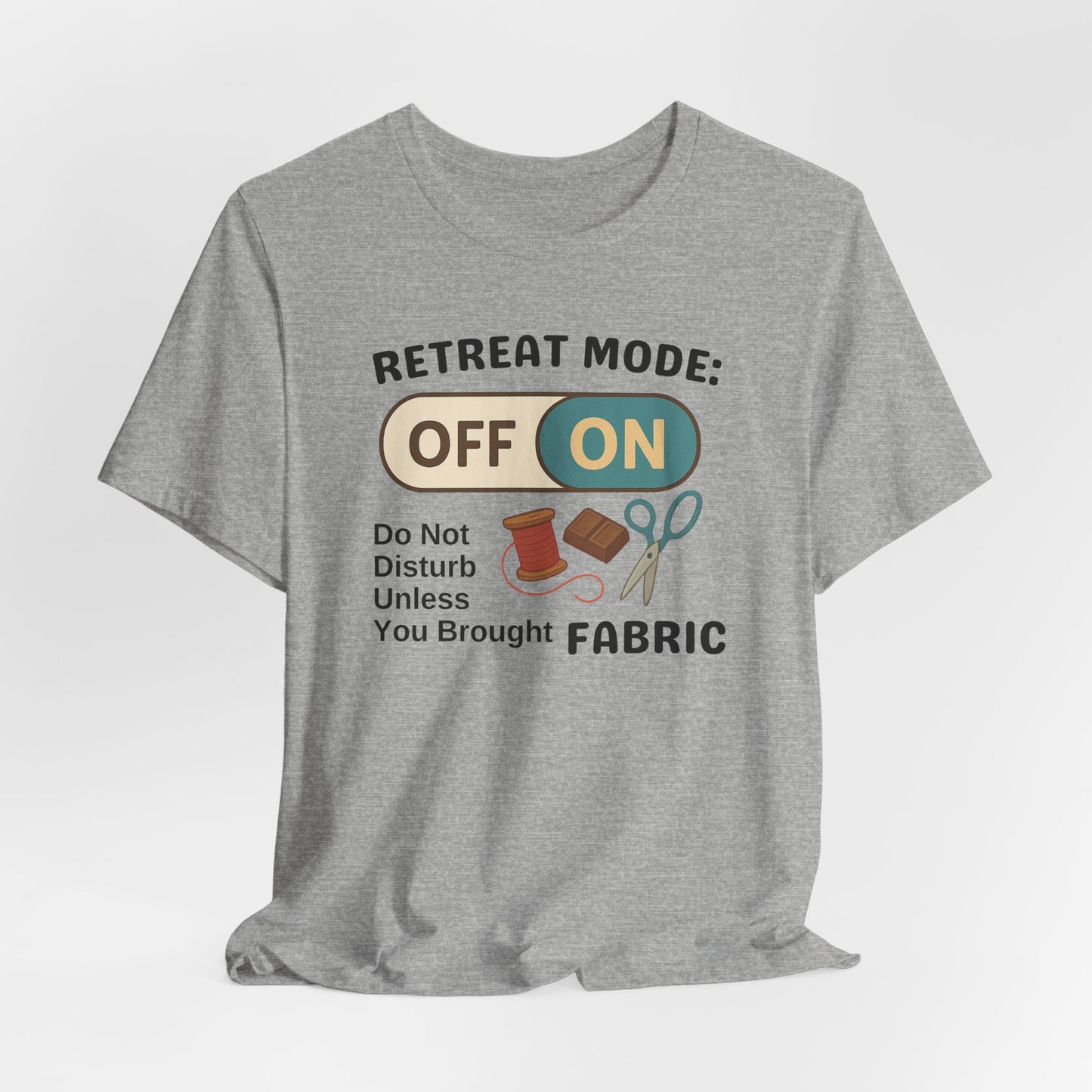 A An Athletic Heather t-shirt with a toggle switch that says "Retreat Mode: OFF/ON" surrounded by a spool of thread, chocolate, and scissors. Text below reads "Do not disturb unless you brought fabric." Fun gift for quilting retreats.