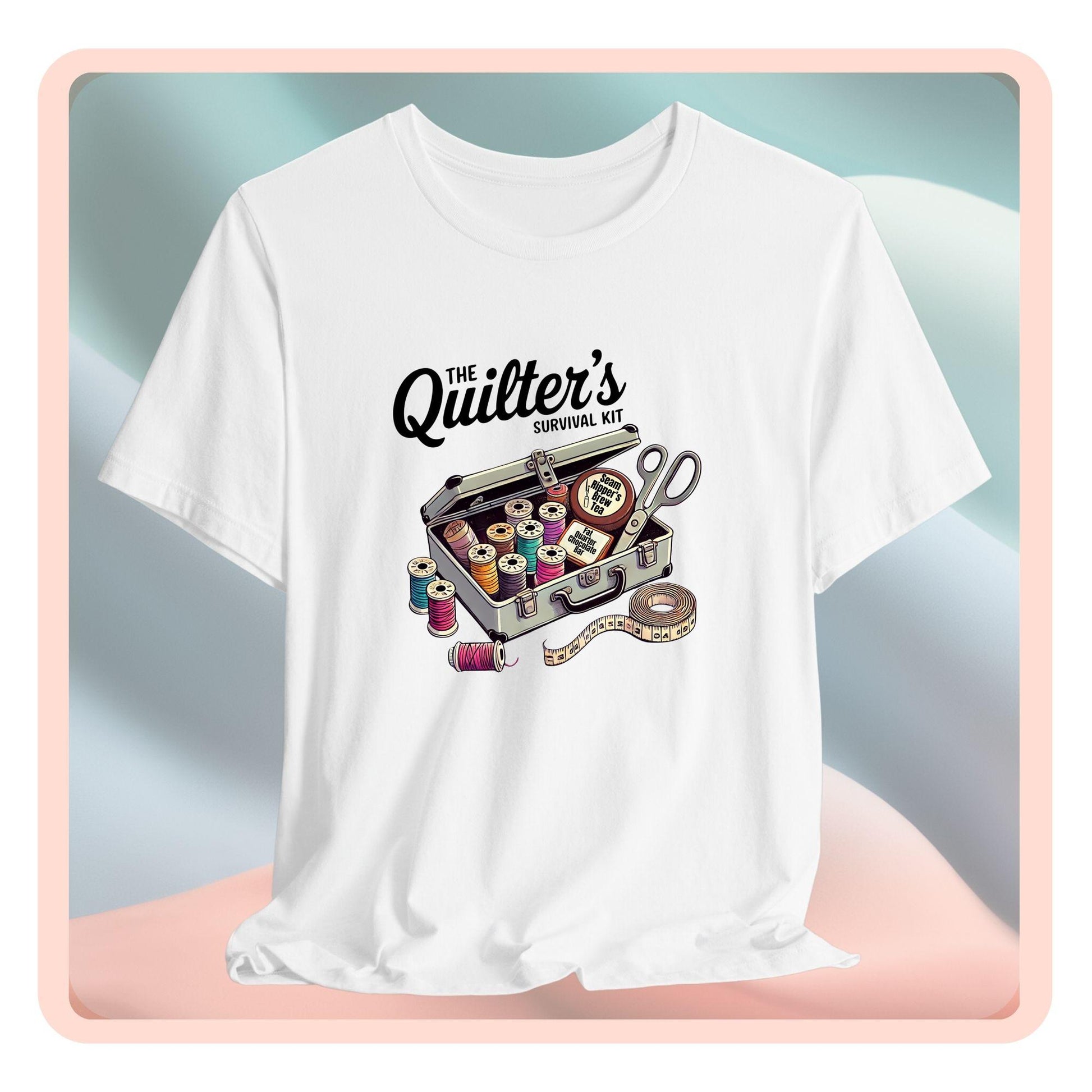 A t-shirt featuring a whimsical illustration of a quilter’s survival kit with colorful thread spools, scissors, and a tape measure, perfect for sewing and quilting enthusiasts.