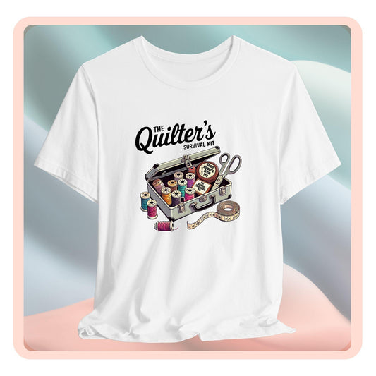 A t-shirt featuring a whimsical illustration of a quilter’s survival kit with colorful thread spools, scissors, and a tape measure, perfect for sewing and quilting enthusiasts.