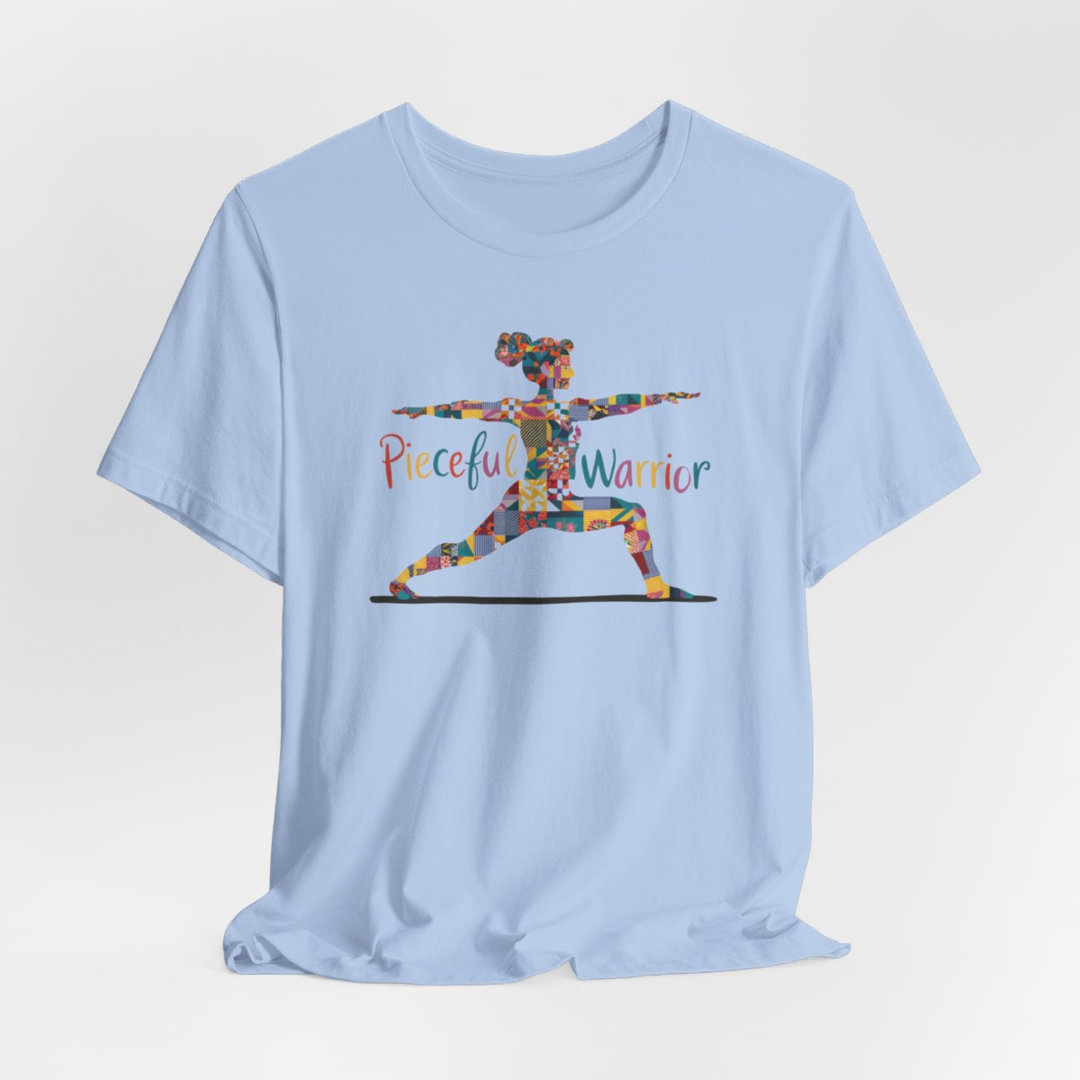 A Baby Blue Tee featuring a colorful patchwork silhouette of woman in yoga warrior pose. Text reads "Pieceful Warrior" in multicolored lettering.