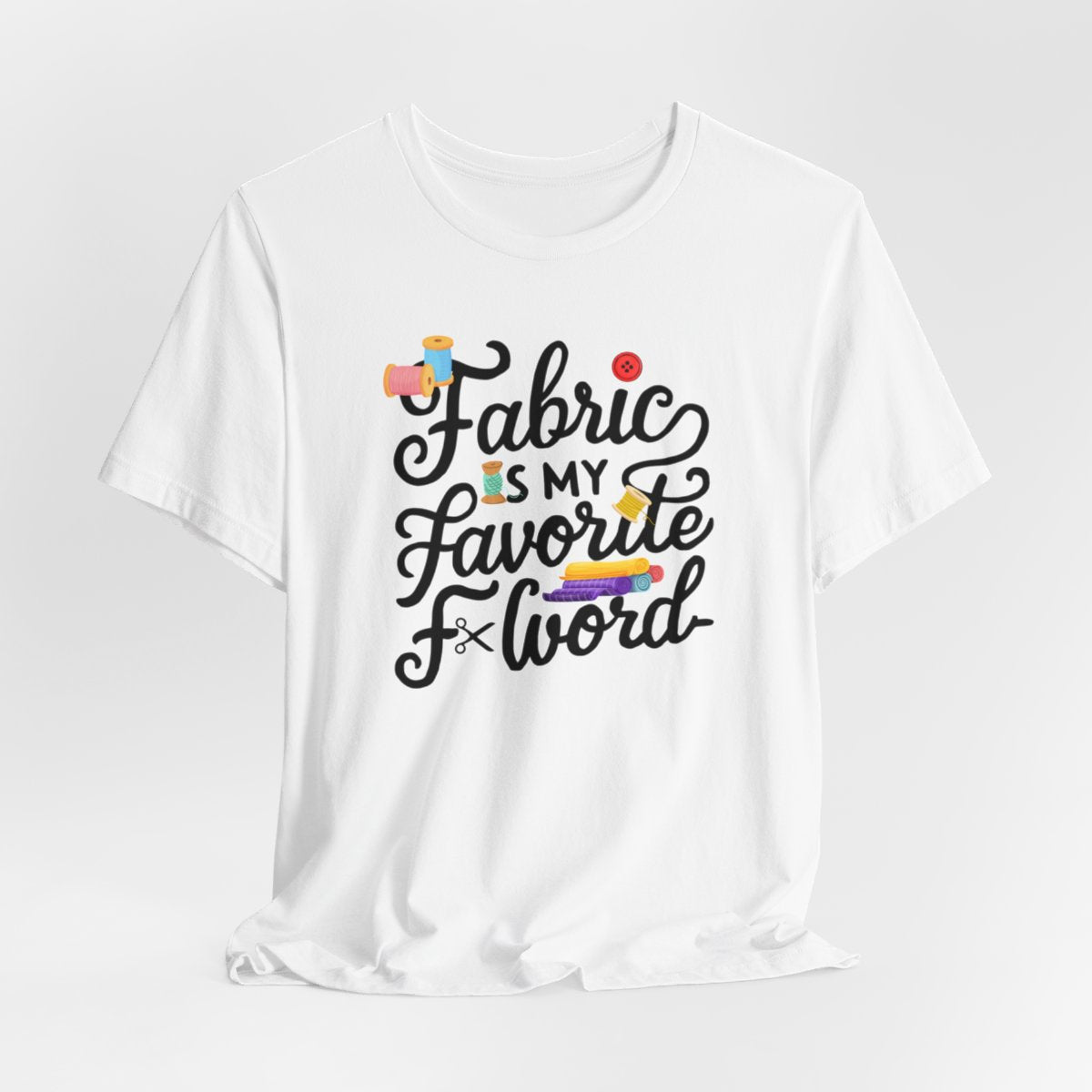 A White T-Shirt with the phrase Fabric is My Favorite F-Word in a bold font with thread, buttons, and fabric bolts