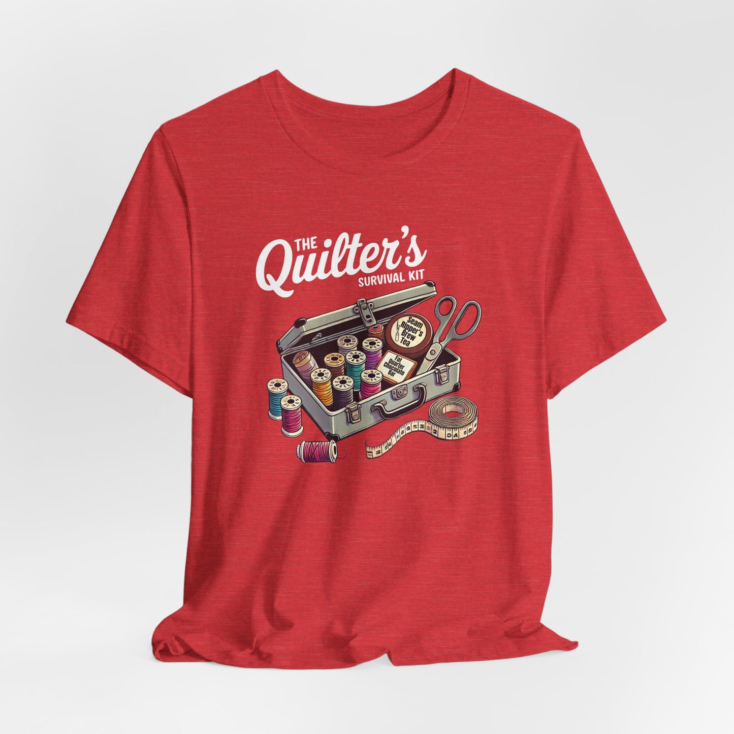 A Heather Red t-shirt featuring a whimsical illustration of a quilter’s survival kit with colorful thread spools, scissors, and a tape measure, perfect for sewing and quilting enthusiasts.