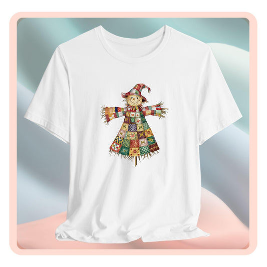 A thanksgiving  quilting t-shirt featuring a smiling scarecrow made entirely of colorful quilt patterns. Wearing a patchwork hat and clothes with various quilt designs. Straw details on hands and neck. Cheerful autumn-themed illustration celebrating quilting craft.