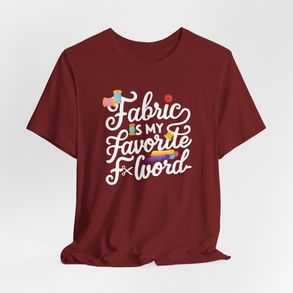 A Cardinal T-Shirt with the phrase Fabric is My Favorite F-Word in a bold font with thread, buttons, and fabric bolts