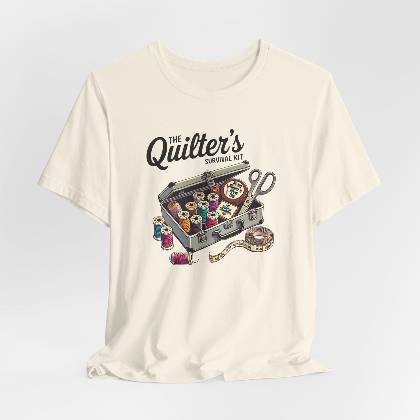 A Natural t-shirt featuring a whimsical illustration of a quilter’s survival kit with colorful thread spools, scissors, and a tape measure, perfect for sewing and quilting enthusiasts.