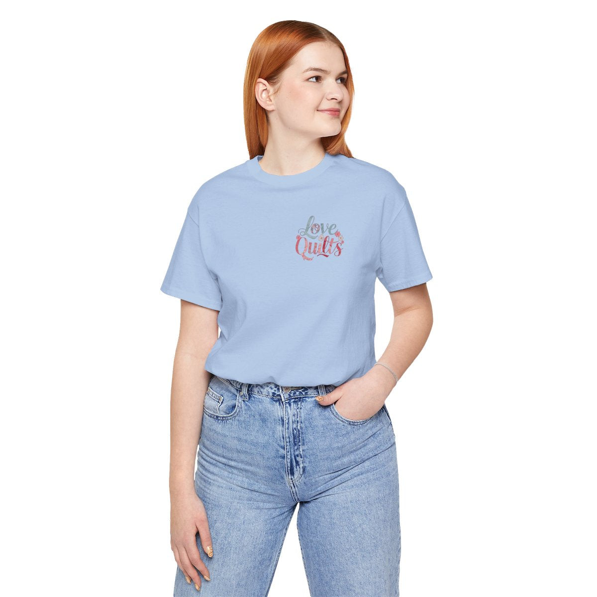 A Baby Blue t-shirt spelling out "Love Quilts". The word "Love" is in teal, while "Quilts" features various shades of pink and red. Small flowers in white and pink adorn the letters, creating a floral and quilting-inspired artwork.