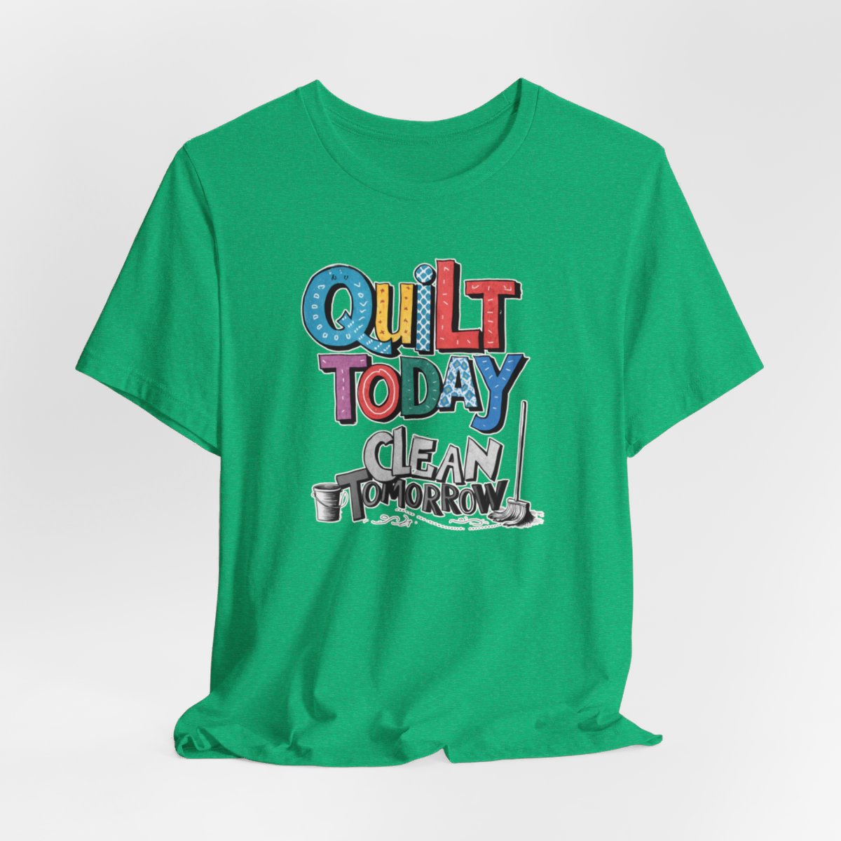 A Heather Kelly funny quilting T-Shirt with the phrase Quilt Today, Clean Tomorrow in a bold and cheerful font with a broom off to the side