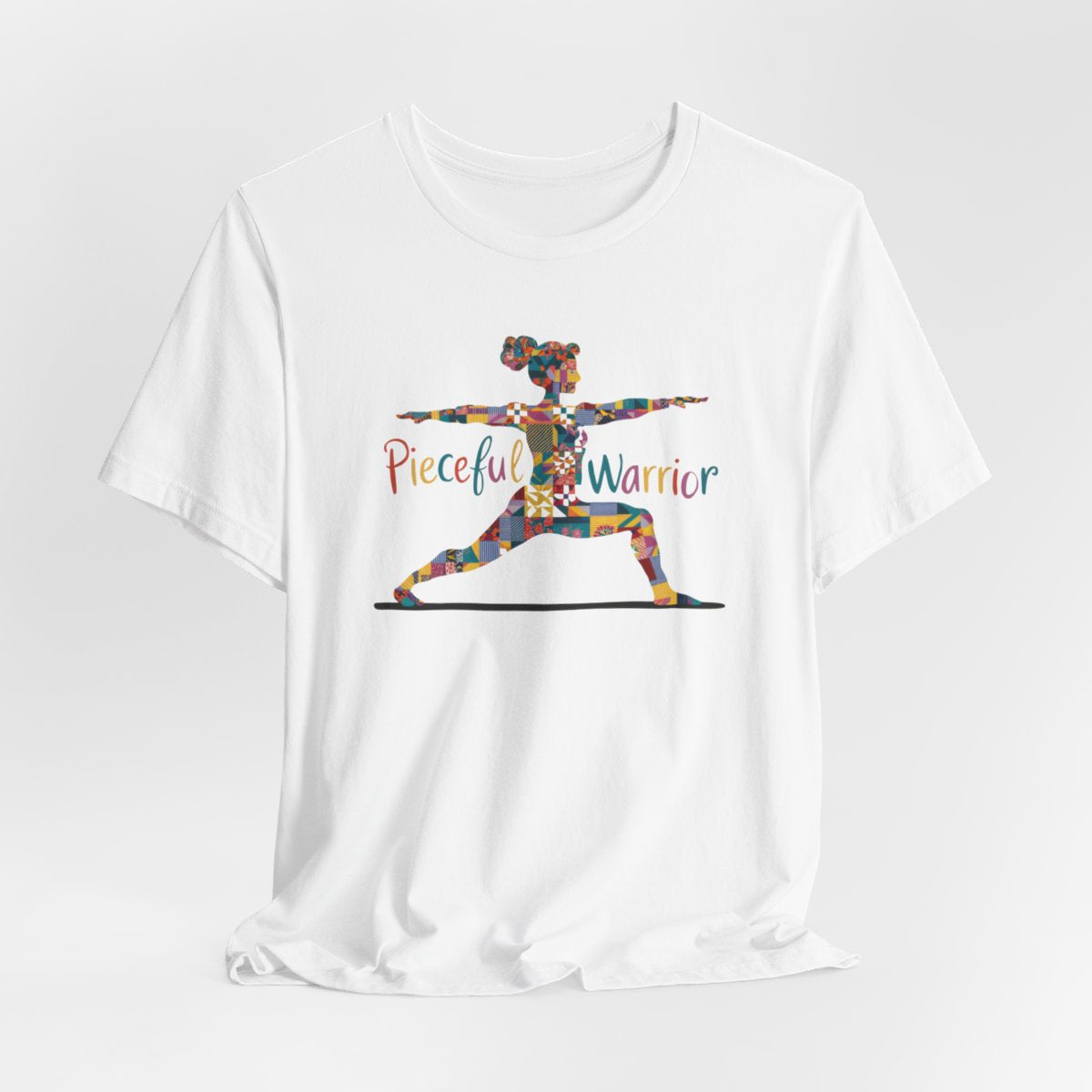 A White Tee featuring a colorful patchwork silhouette of woman in yoga warrior pose. Text reads "Pieceful Warrior" in multicolored lettering.