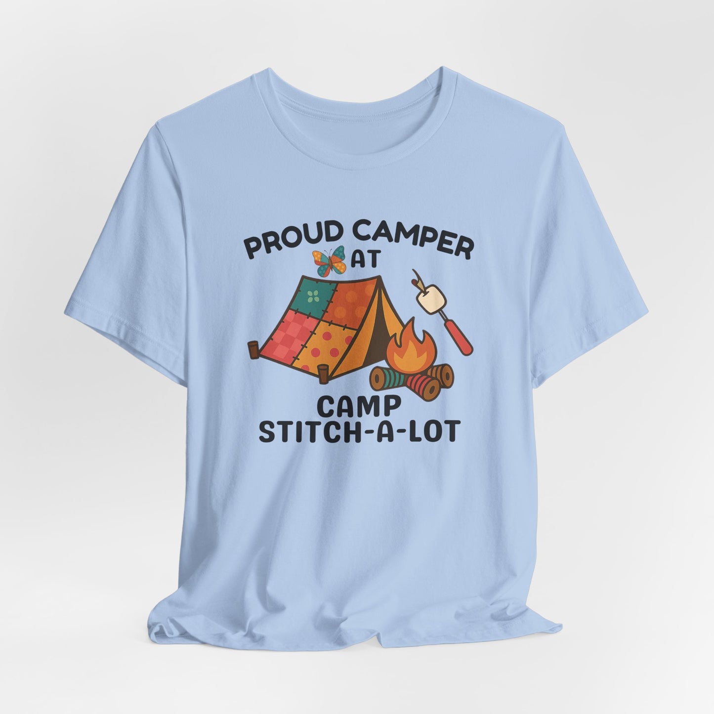 A A Baby Blue t-shirt featuring a colorful design with a patchwork tent, thread spool campfire, marshmallow on a seam ripper stick, and a butterfly. Text reads "Proud Camper at Camp Stitch-a-Lot." Fun gift for quilting retreats.