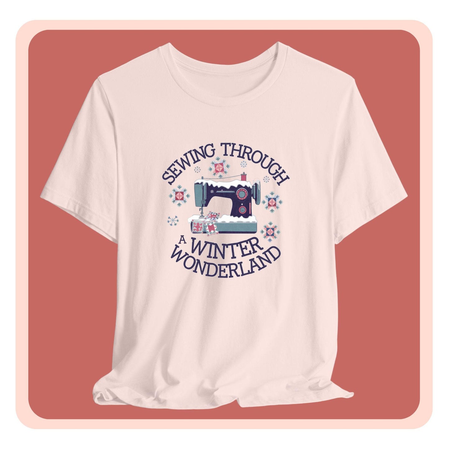 A winter quilting t-shirt featuring  a sewing machine covered in snow, surrounded by quilted snowflakes, with the phrase "Sewing Through a Winter Wonderland" above and below the image.