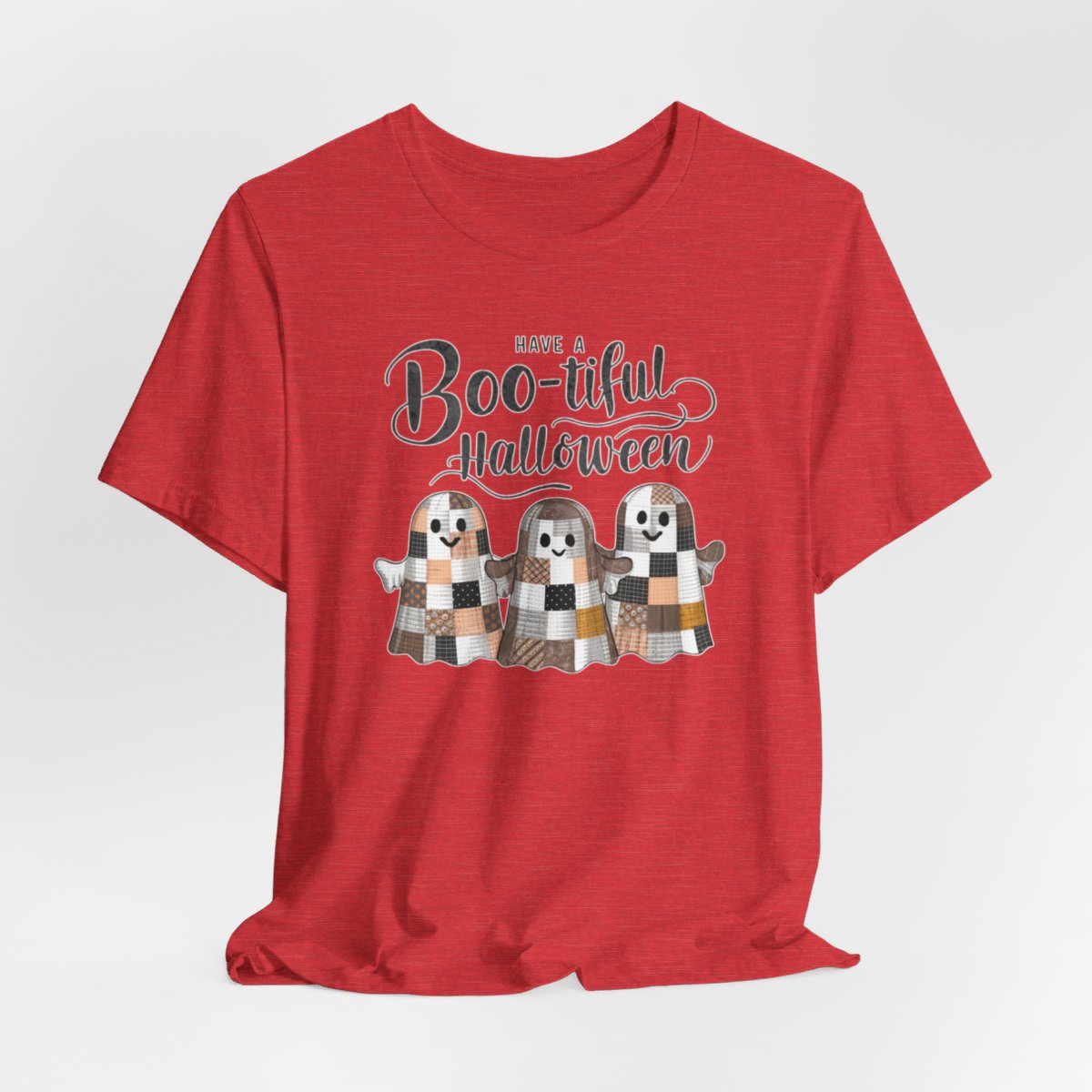 A Heather Red Halloween Quilting T-Shirt featuring three smiling patchwork ghosts made of various quilt patterns in autumn colors. Text reads "Have a Boo-tiful Halloween" in stylized lettering. Perfect for quilters who love Halloween.