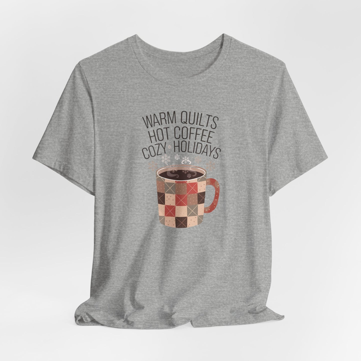 An Athletic Heather christmas quilting t-shirt featuring a cozy patchwork quilt-themed coffee mug, surrounded by snowflakes, with the phrase "Warm Quilts, Hot Coffee, Cozy Holidays" above the mug, celebrating the warmth of quilts and coffee during the holiday season.