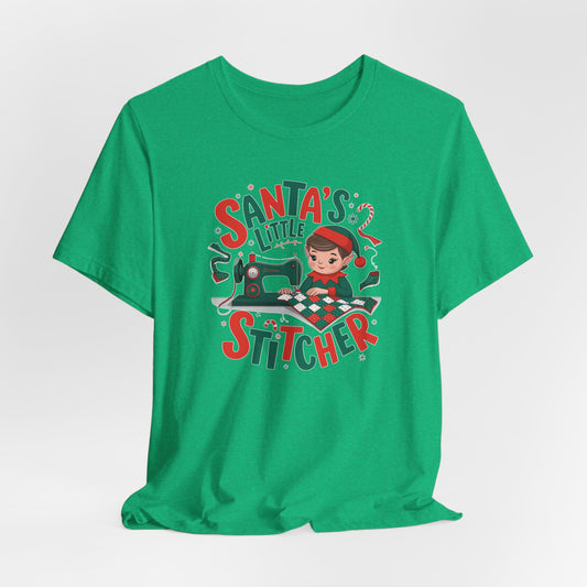 A Heather Kelly christmas quilting t-shirt featuring an adorable elf is sewing a festive patchwork quilt on a sewing machine, surrounded by holiday-themed decorations, with the phrase "Santa's Little Stitcher" above and below the design.