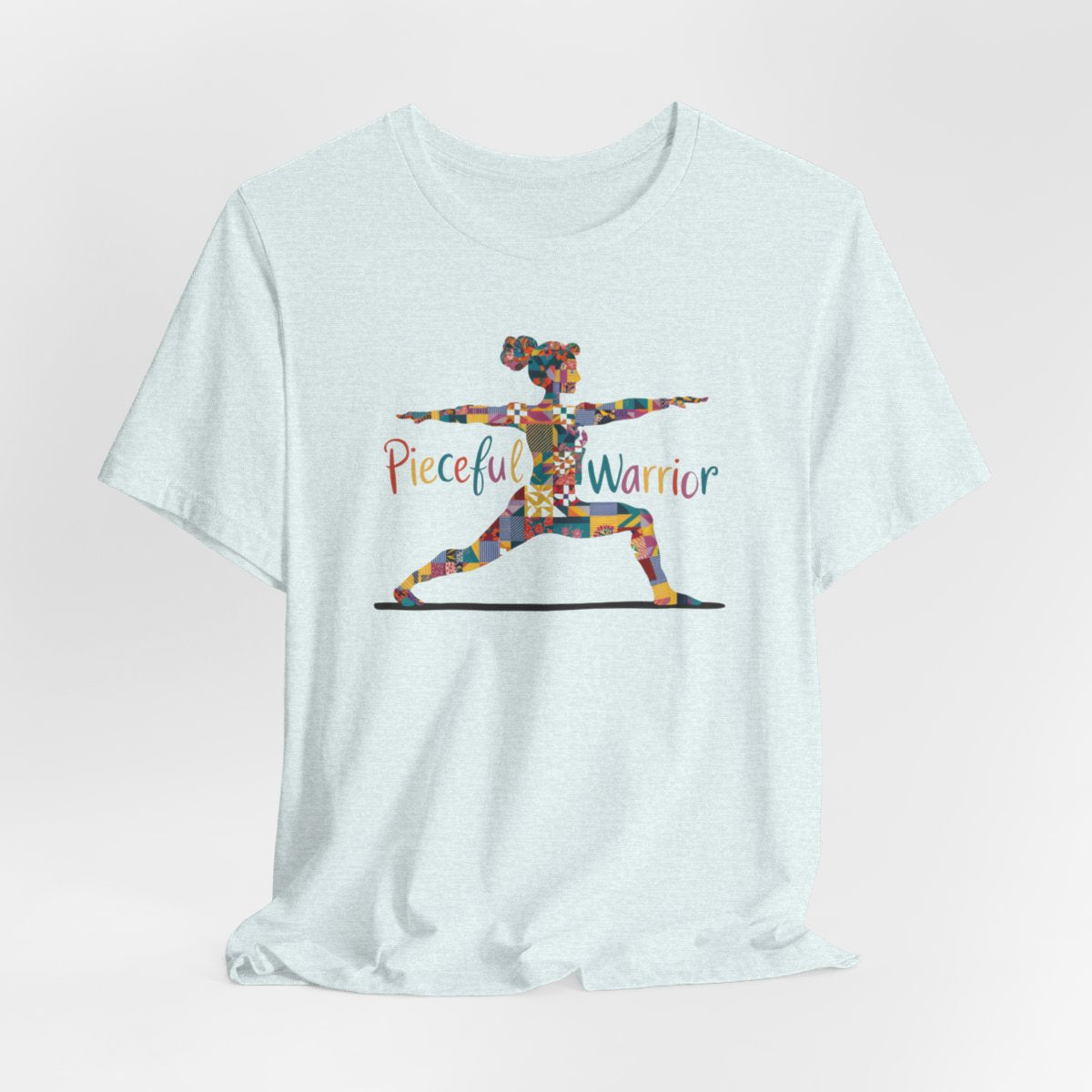 A Heather Ice Blue Tee featuring a colorful patchwork silhouette of woman in yoga warrior pose. Text reads "Pieceful Warrior" in multicolored lettering.