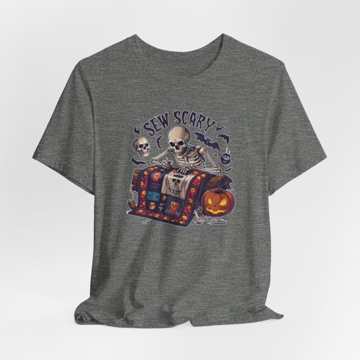 A Deep Heather Halloween Quilting T-Shirt featuring a skeleton sewing Halloween quilt. Colorful patchwork with spooky motifs. Bats and pumpkins surround skeleton. Text reads "Sew Scary". Ideal for quilters who love Halloween.