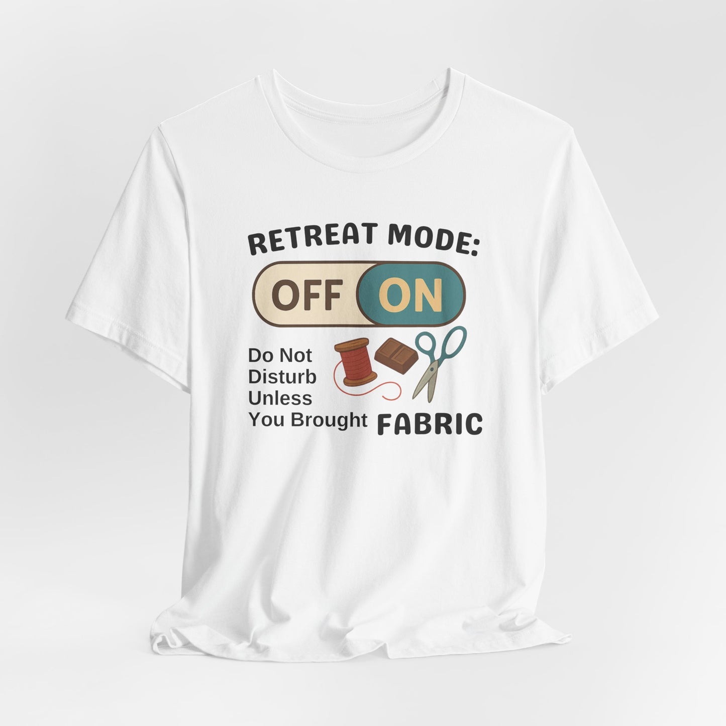 A A White t-shirt with a toggle switch that says "Retreat Mode: OFF/ON" surrounded by a spool of thread, chocolate, and scissors. Text below reads "Do not disturb unless you brought fabric." Fun gift for quilting retreats.