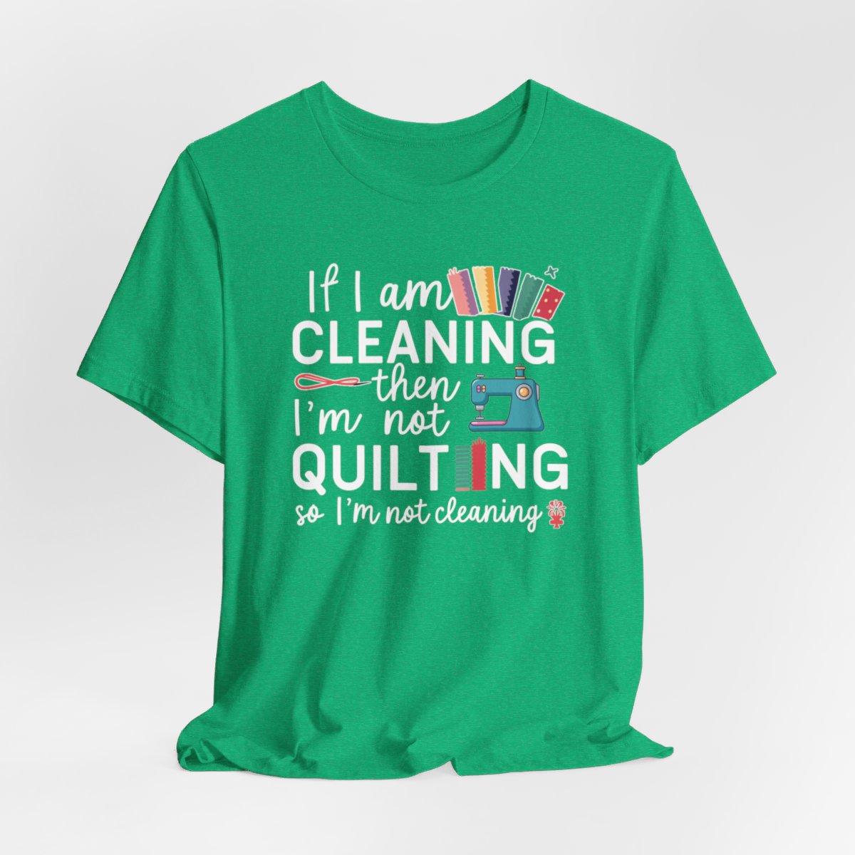 A Heather Kelly funny quilting T-Shirt with the phrase If I am Cleaning then I'm not Quilting in a bold and cheerful font with images of quilting icons and supplies