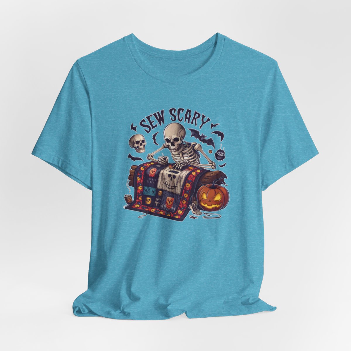 A Heather Aqua Halloween Quilting T-Shirt featuring a skeleton sewing Halloween quilt. Colorful patchwork with spooky motifs. Bats and pumpkins surround skeleton. Text reads "Sew Scary". Ideal for quilters who love Halloween.