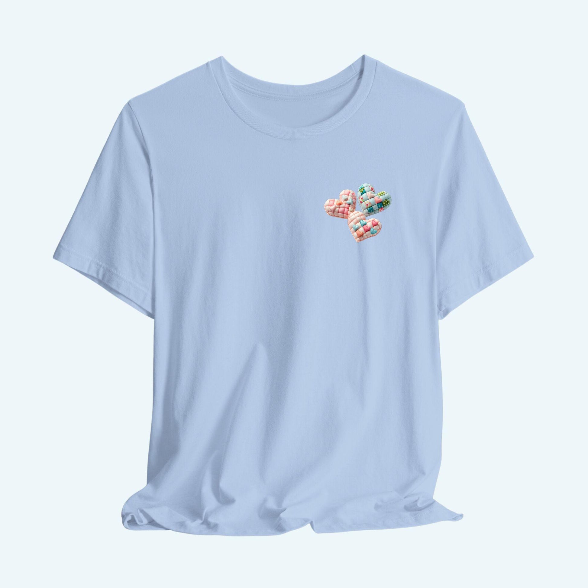 A Tshirt featuring Three heart-shaped quilted designs arranged together. Each heart features different quilting patterns and textures, including patchwork, floral prints, and tiny embroidered hearts. The hearts are in pastel shades of pink and blue, with white accents.