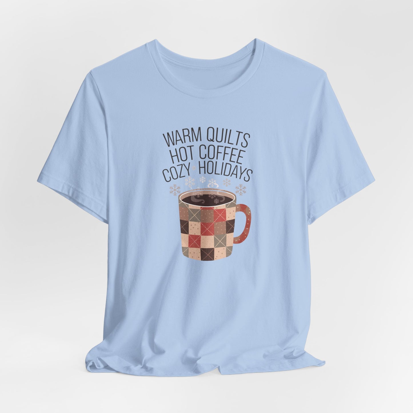 A Baby Blue christmas quilting t-shirt featuring a cozy patchwork quilt-themed coffee mug, surrounded by snowflakes, with the phrase "Warm Quilts, Hot Coffee, Cozy Holidays" above the mug, celebrating the warmth of quilts and coffee during the holiday season.