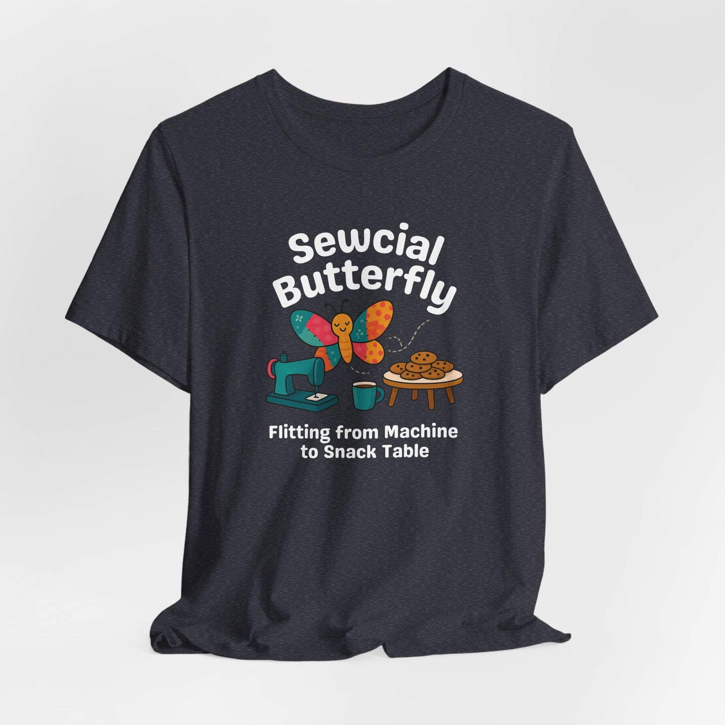 A A Heather Navy t-shirt with a colorful design showing a patchwork butterfly flying between a sewing machine and a table of cookies. Text reads “Sewcial Butterfly – Flitting from Machine to Snack Table.” Funny gift for quilters
