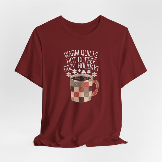 A Cardinal christmas quilting t-shirt featuring a cozy patchwork quilt-themed coffee mug, surrounded by snowflakes, with the phrase "Warm Quilts, Hot Coffee, Cozy Holidays" above the mug, celebrating the warmth of quilts and coffee during the holiday season.