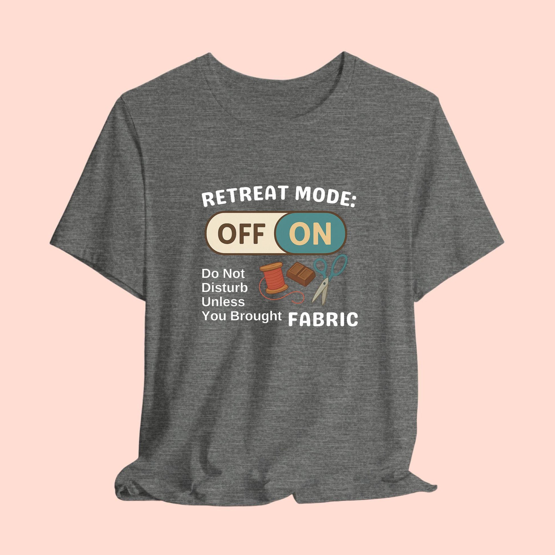 A A t-shirt with a toggle switch that says "Retreat Mode: OFF/ON" surrounded by a spool of thread, chocolate, and scissors. Text below reads "Do not disturb unless you brought fabric." Fun gift for quilting retreats.