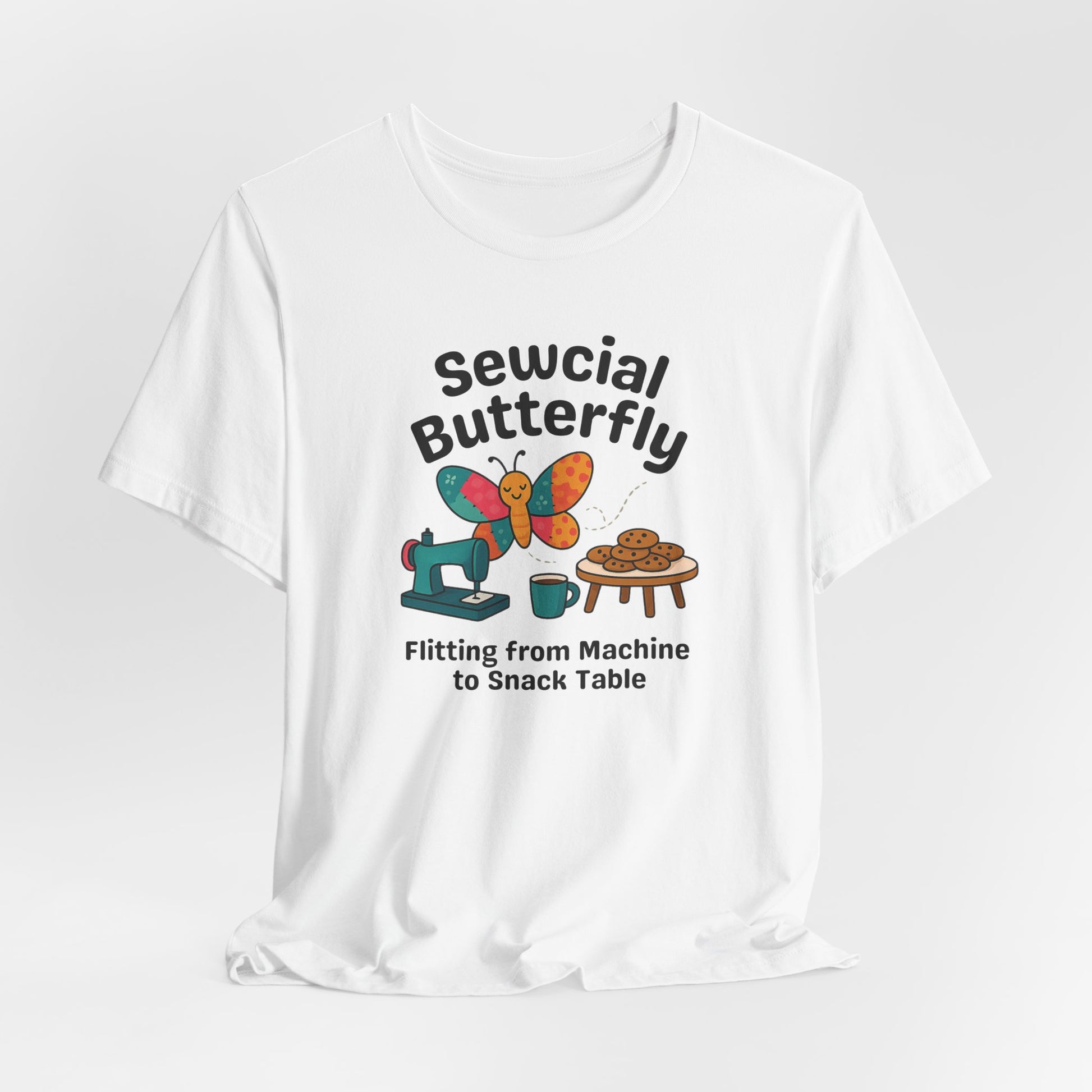 A A White t-shirt with a colorful design showing a patchwork butterfly flying between a sewing machine and a table of cookies. Text reads “Sewcial Butterfly – Flitting from Machine to Snack Table.” Funny gift for quilters