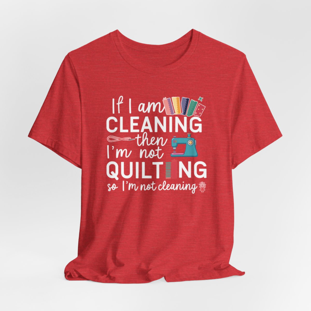 A Heather Red funny quilting T-Shirt with the phrase If I am Cleaning then I'm not Quilting in a bold and cheerful font with images of quilting icons and supplies