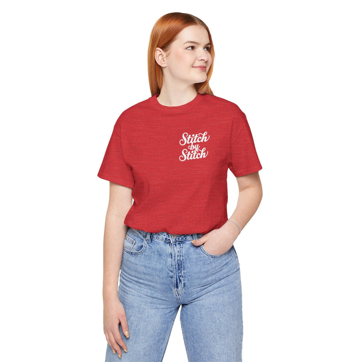 A Heather Red T-Shirt featuring the phrase "Stitch by Stitch". The word "Stitch" is written twice in a flowing script font, while "by" is centered between them in a smaller, sans-serif font. The design has a clean, minimalist aesthetic.
