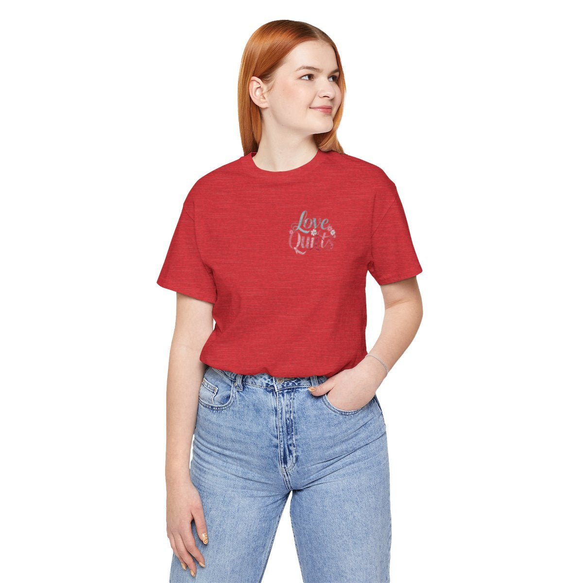 A Heather Red t-shirt spelling out "Love Quilts". The word "Love" is in teal, while "Quilts" features various shades of pink and red. Small flowers in white and pink adorn the letters, creating a floral and quilting-inspired artwork.