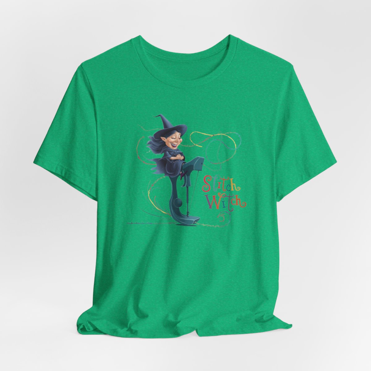 A Heather Kelly T-shirt with a cartoon illustration of a smiling witch with pointed hat riding a teal sewing machine. Colorful stitches swirl around her in the air. Text reads "Stitch Witch" in playful, multicolored letters.