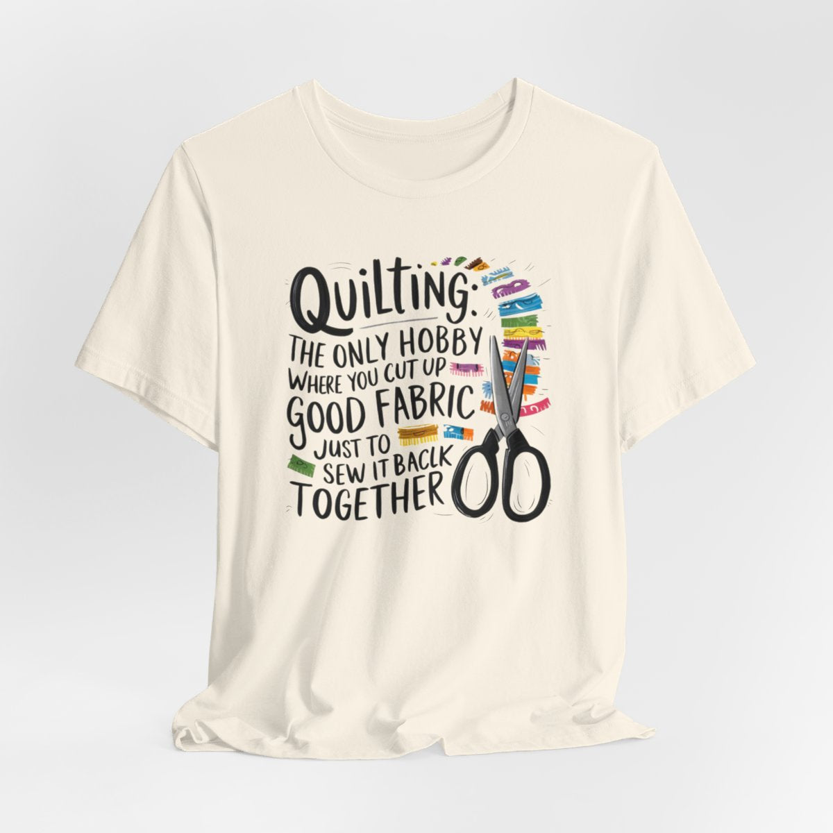 A Natural Quilting-themed T-Shirt with text "Quilting: The Only Hobby Where You Cut Up Good Fabric Just to Sew it Back Together" surrounded by colorful fabric scraps and scissors.