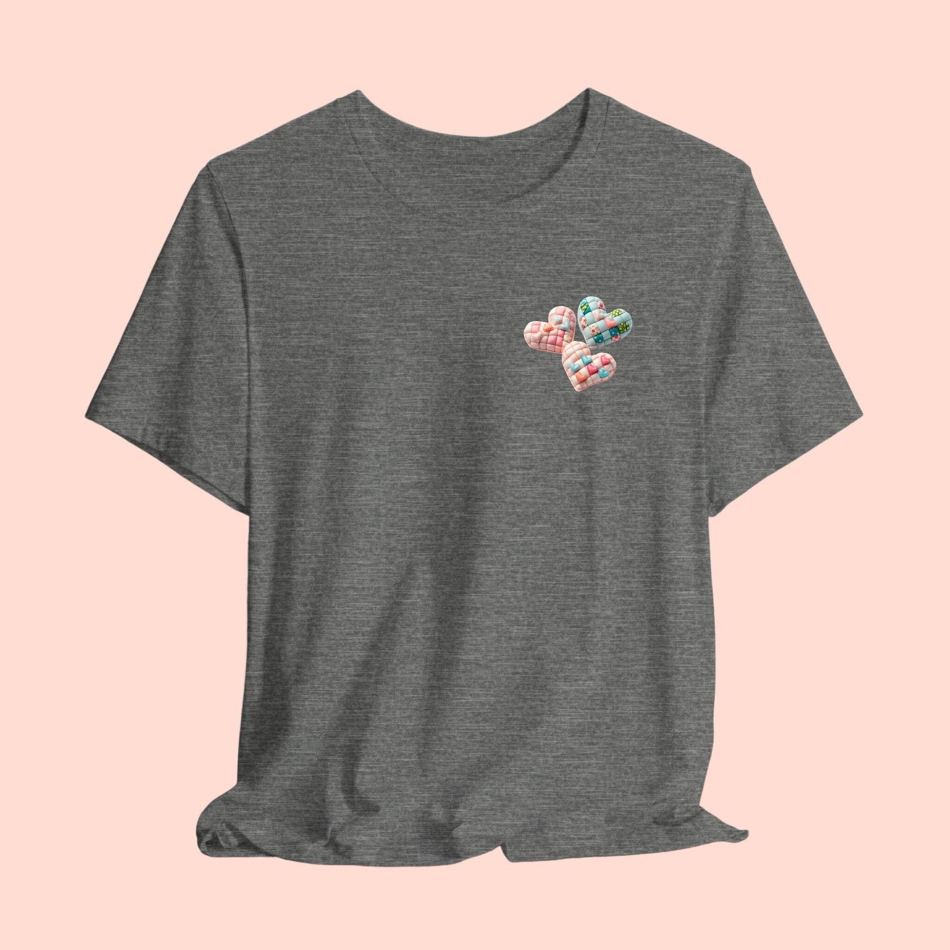 A Tshirt featuring Three heart-shaped quilted designs arranged together. Each heart features different quilting patterns and textures, including patchwork, floral prints, and tiny embroidered hearts. The hearts are in pastel shades of pink and blue, with white accents.